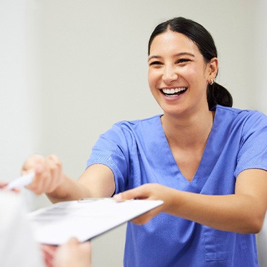 Dental assistant smiling while handing patient form