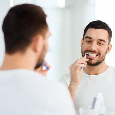 Man in white shirt smiling while brushing his teeth