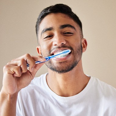 Man smiling while brushing his teeth