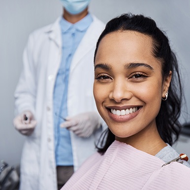 A smiling young woman with a masked dentist in the background