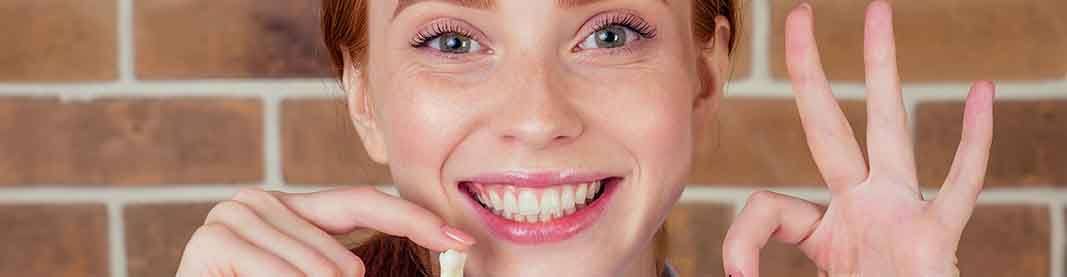 Woman with red hair in front of brick wall smiling while giving OK hand sign and holding extracted tooth