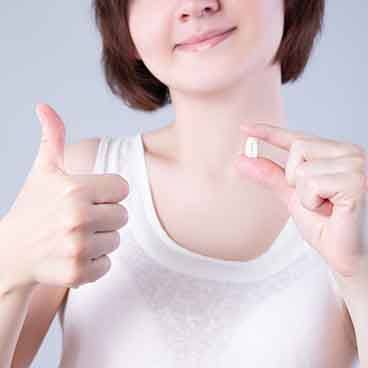 Nose-to-chest view of a woman holding extracted tooth in one hand and giving thumbs up with other