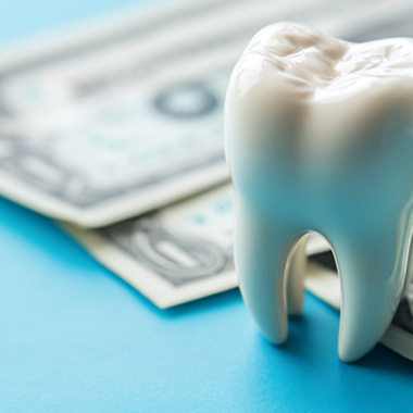 Model tooth next to dollars bills on blue surface